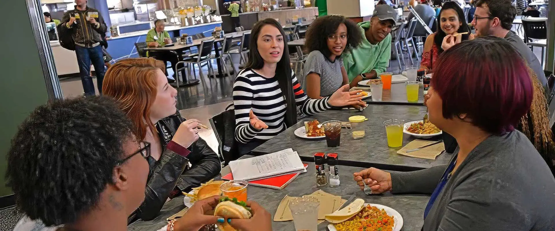 Students sitting around table in dining hall eating and having a conversation